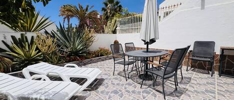 Un patio con sillones, una mesa y sillas, rodeado de cactus y palmeras.