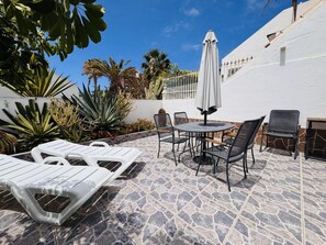 A patio with lounge chairs, a table, and chairs, surrounded by cacti and palm trees. - Sunny Villa Holiday Home (Torviscas Bajo)