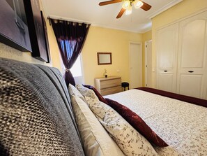 A bedroom with a bed, a dresser, a mirror, and a ceiling fan.