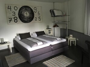 A modern bedroom with a double bed, bedside tables, a lamp, a shelf with a pillow, and a wall clock.