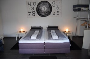 A double bed with a grey and white striped duvet, two bedside tables with lamps, and a wall with a large abstract number painting.