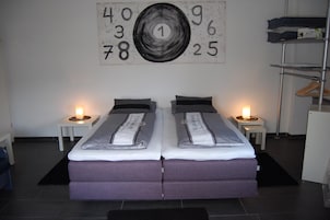 A double bed with a grey and white striped duvet, two bedside tables with lamps, and a wall with a large abstract number painting.