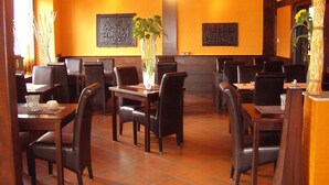 Interior de restaurante con mesas y sillas de madera, un jarrón con girasoles y decoración en la pared.