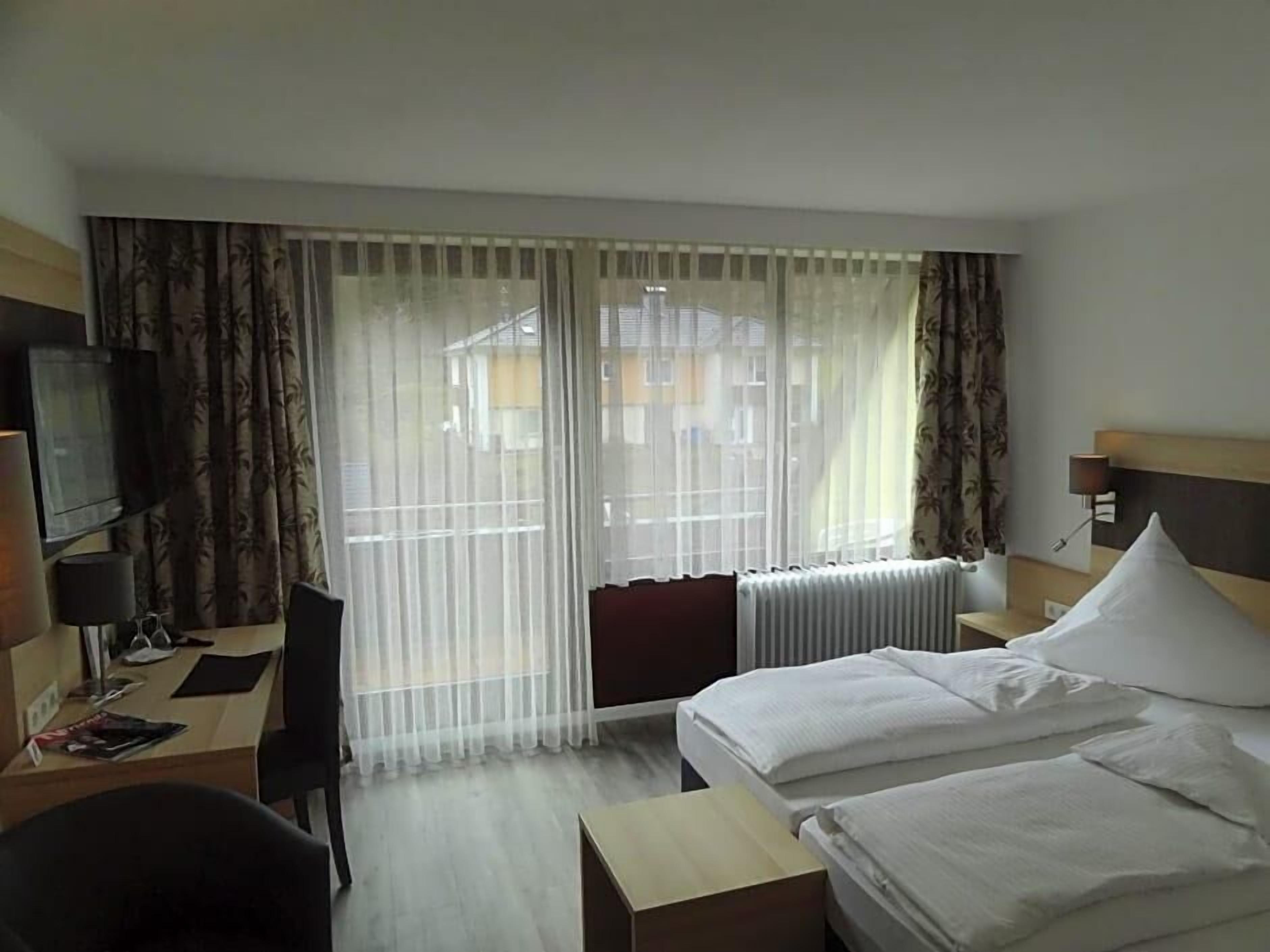 Ein Hotelzimmer mit Bett, Schreibtisch, Stuhl, Fernseher und einem Fenster mit Vorhängen.