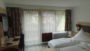 Ein Hotelzimmer mit Bett, Schreibtisch, Stuhl, Fernseher und einem Fenster mit Vorhängen.