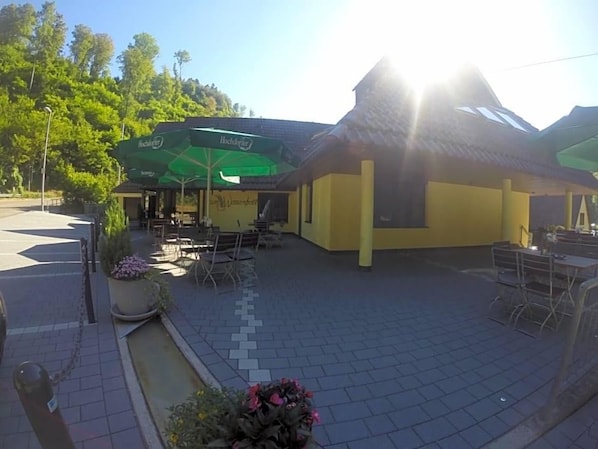 An outdoor seating area with tables and chairs, a building with a yellow facade, and a green awning.