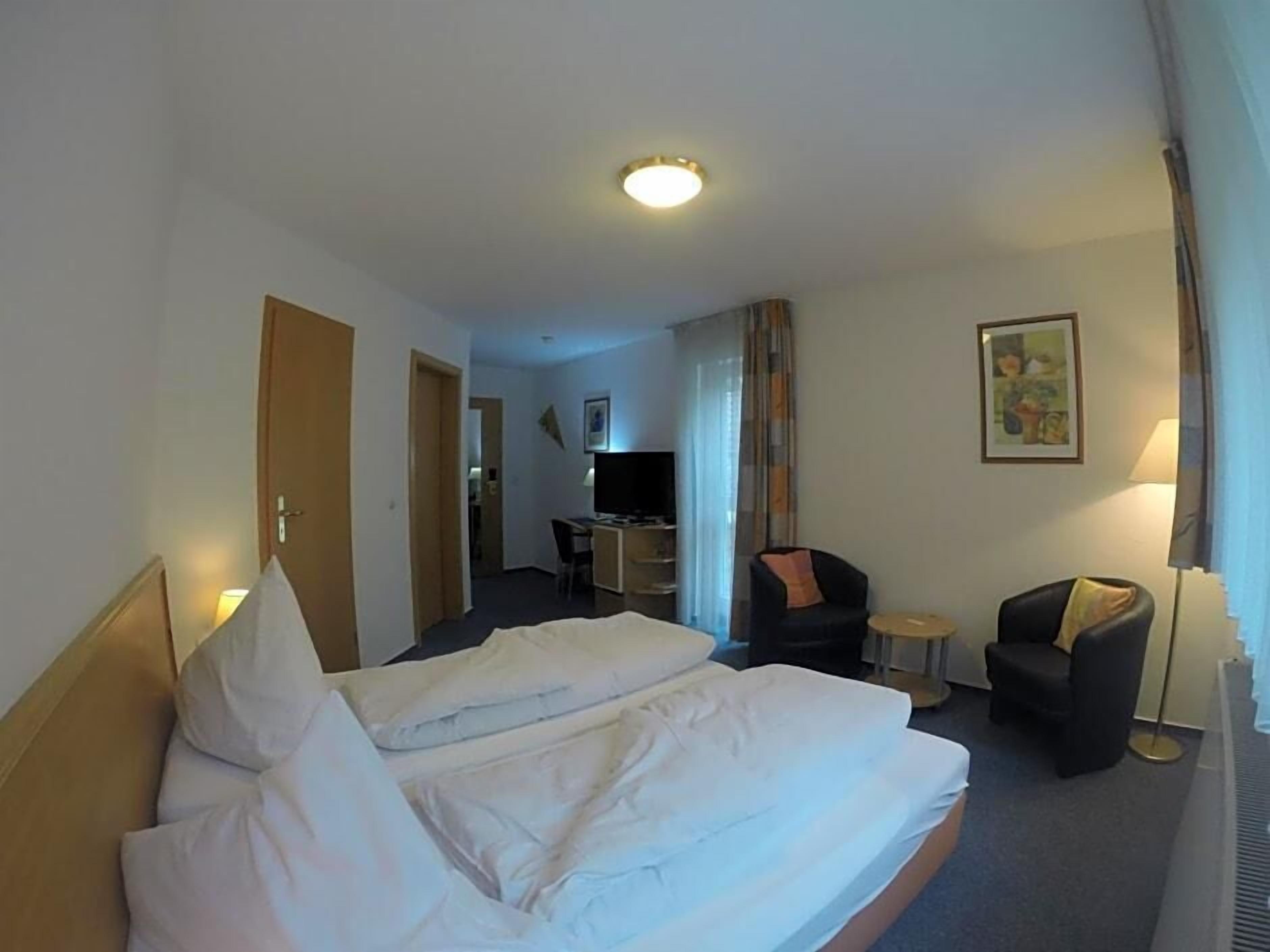 A hotel room with a bed, a desk, a chair, and a lamp.