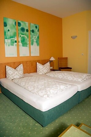 Cama doble con cabecera tapizada de verde, dos almohadas y una mesita de noche con lámpara.