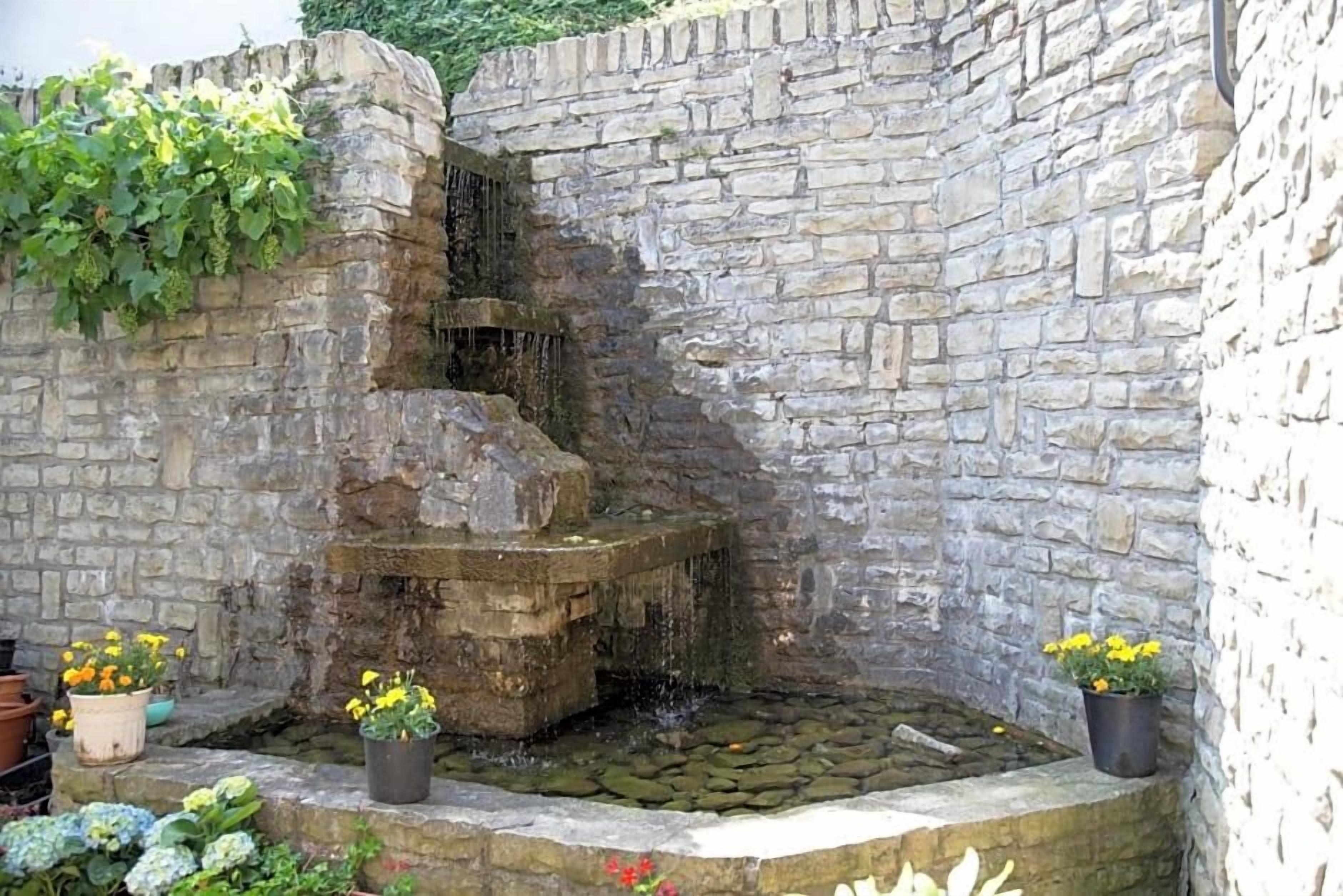 Eine Steinsäule mit Wasserspiel und Pflanzgefäßen.
