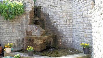 Eine Steinsäule mit Wasserspiel und Pflanzgefäßen.