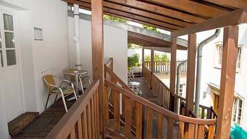 Una escalera de madera lleva a un espacio exterior cubierto con barandilla, una silla y una mesa.