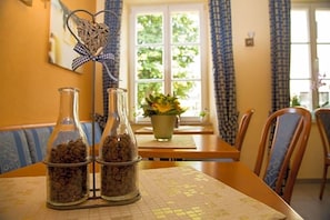 A dining area with a table set for two, featuring a patterned tablecloth and a window with curtains.