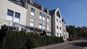 A multi-story hotel with a flat roof, large windows, and a well-maintained hedge along the street.