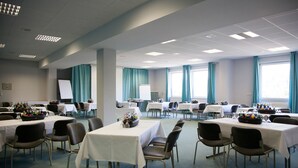 A conference room with multiple tables and chairs, white tablecloths, and teal curtains.