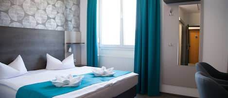 A hotel room with a large bed, a headboard, a window with curtains, a mirror, and a chair.