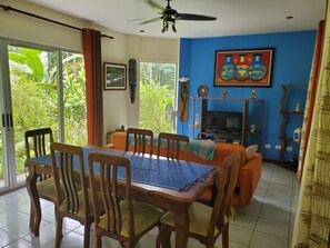 Un coin repas avec une table et des chaises, un téléviseur et un mur bleu orné d’un tableau.