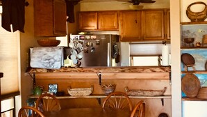 Une cuisine avec des meubles en bois, un plan de travail en marbre, une table à manger avec des chaises en osier et un ventilateur de plafond.