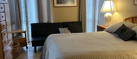 A hotel room with a bed, a desk, a chair, a dresser, a lamp, and a ceiling fan.