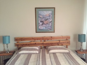 A bedroom with a wooden headboard, two bedside tables with lamps, and a framed artwork on the wall.