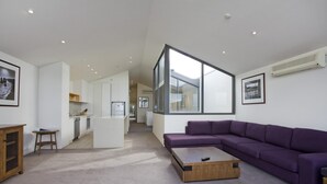 Una sala moderna con un sofá morado, una mesa de centro de madera y una cocina al fondo.