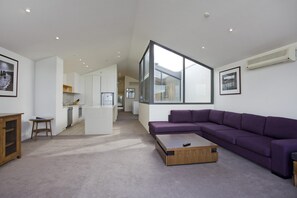 Ein modernes Wohnzimmer mit einem violetten Sofa, einem Holztisch und einer Küche im Hintergrund.