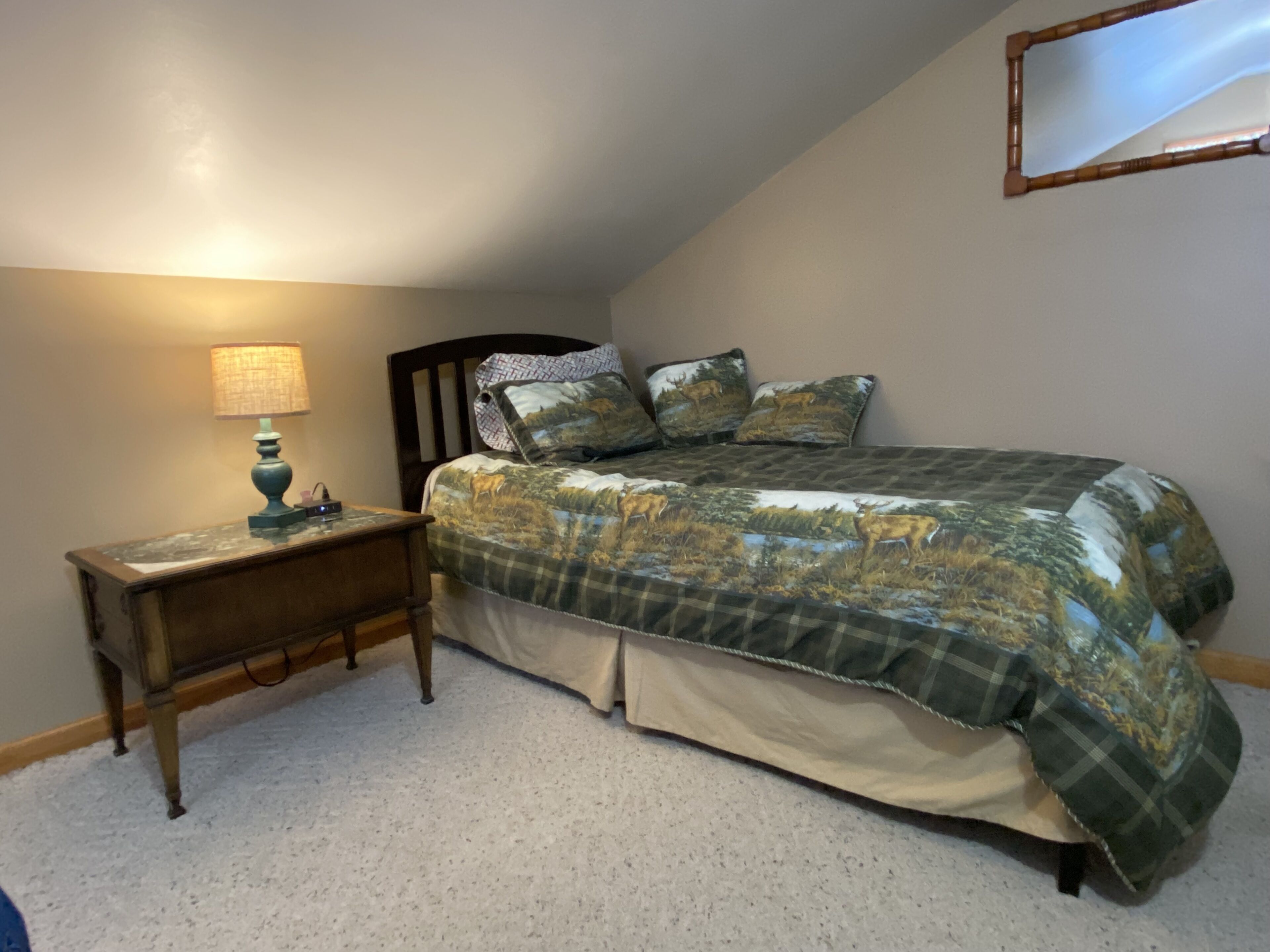 A bedroom with a bed, a nightstand, a lamp, and a mirror on the wall.
