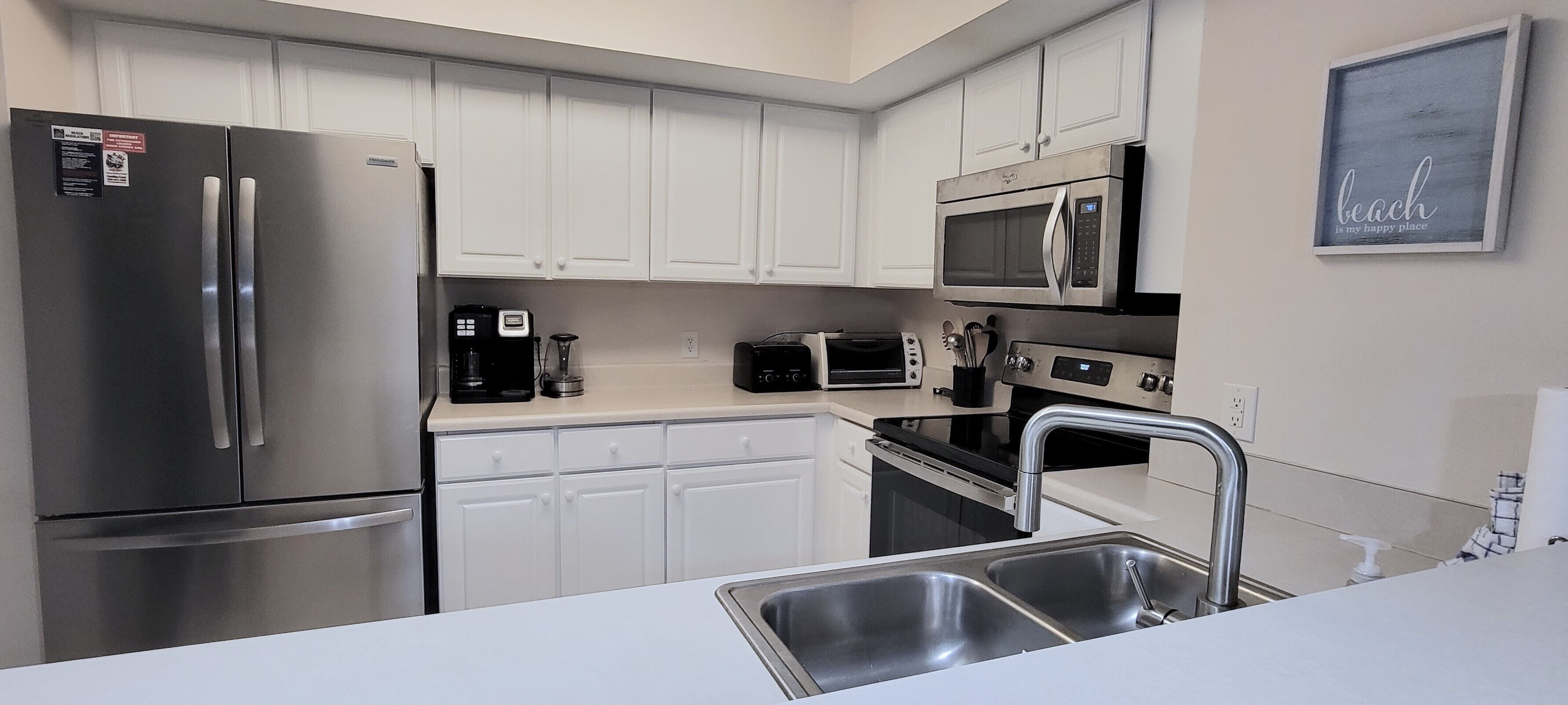 A modern kitchen with stainless steel appliances, white cabinetry, and a double sink.