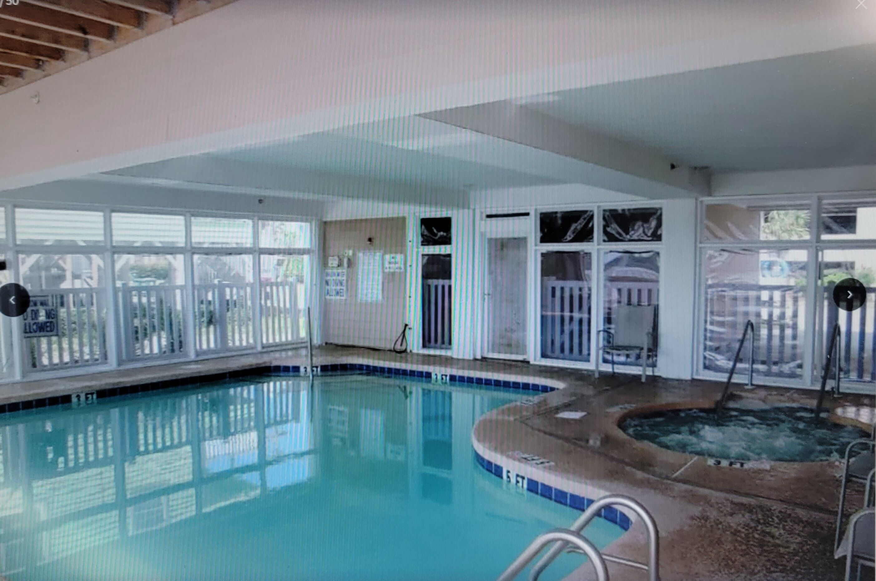 Una piscina interior con un jacuzzi, paredes de vidrio transparente y un área cercada.