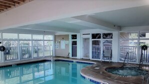 Piscina interna com banheira de hidromassagem, paredes de vidro transparente e área cercada.