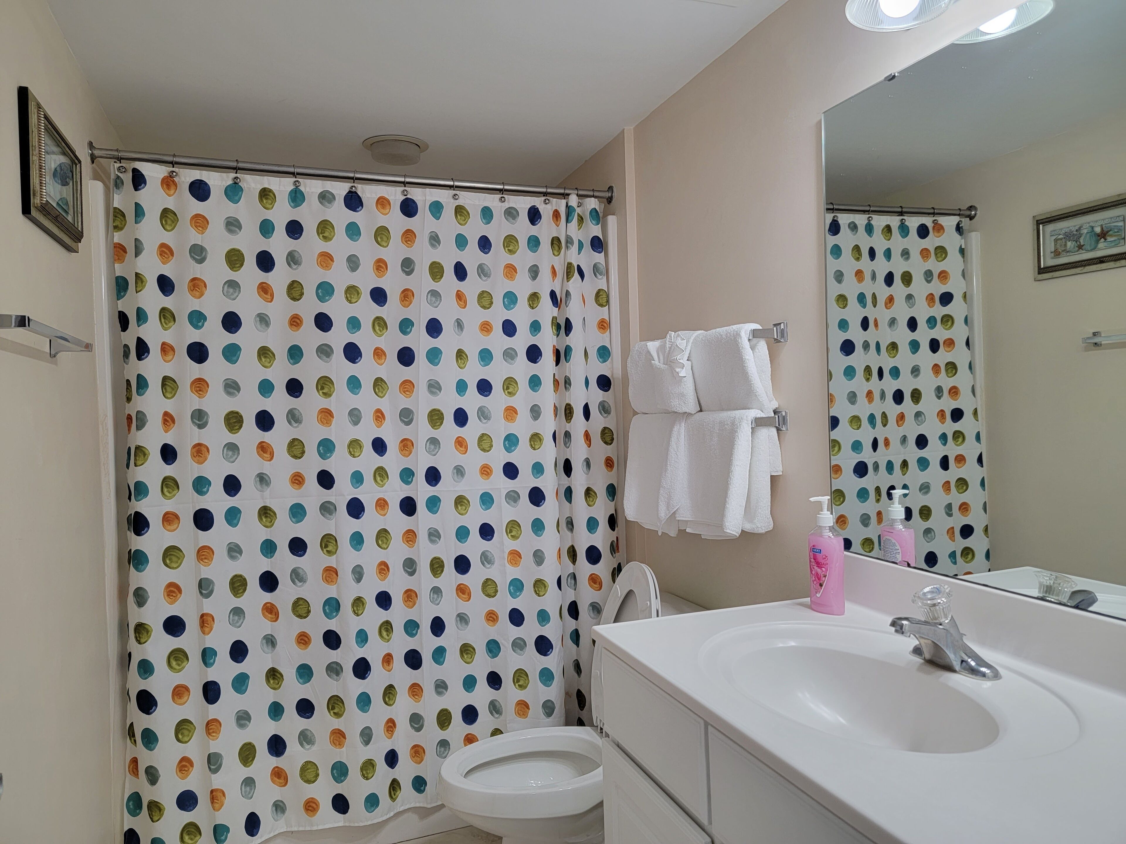 Ein Badezimmer mit einem Vorhang mit Punkten, einer Toilette, einem Waschbecken mit Spiegel und einem Handtuchhalter mit zwei Handtüchern.
