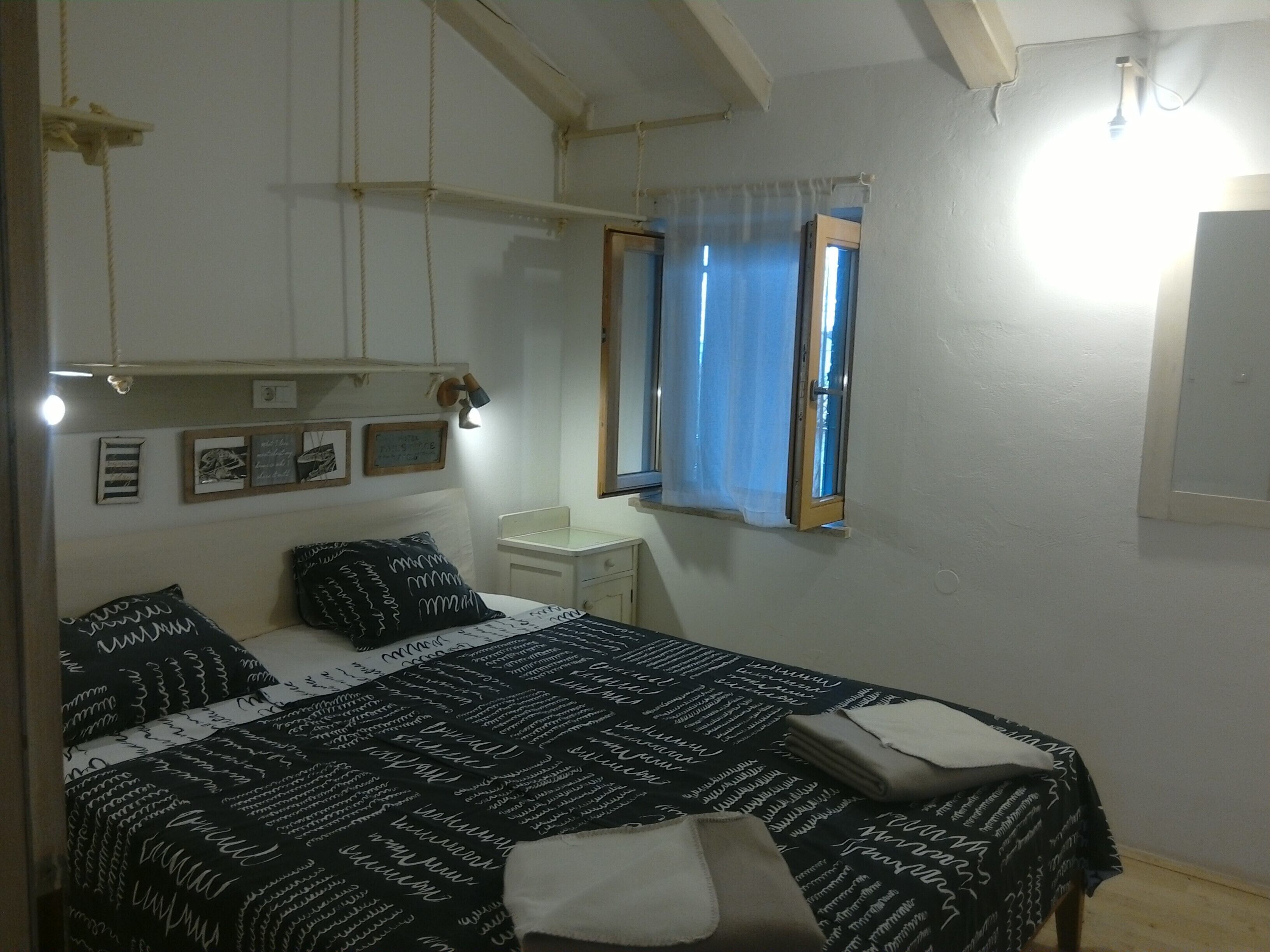 Een slaapkamer met een bed, nachtkastjes, een raam met gordijnen en wandlampen.