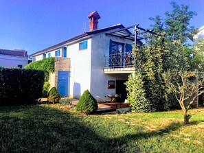 A two-story house with a blue door, a balcony, and a small garden area.