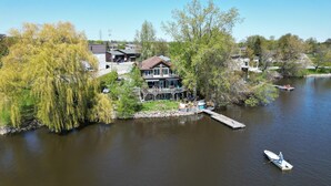 A lakeside house with a dock, surrounded by trees and a clear sky.