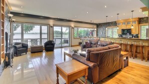 A spacious living room with a leather sofa, wooden coffee table, and a view of a lake through large windows.