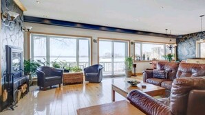 A spacious living room with a fireplace, leather sofa, and large windows overlooking a body of water.
