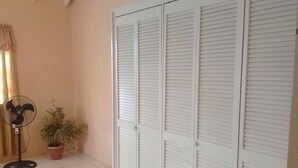 Ein Zimmer mit weiß gefliestem Boden, einem Blumentopf, einem Standventilator und einer Reihe weißer, abgekanteter Türen.