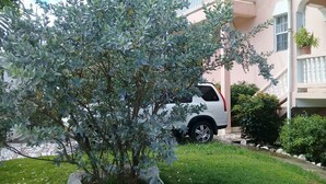 Ein weißer SUV vor einem Gebäude mit Balkon und einem Baum im Vordergrund.