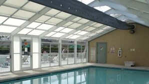 An indoor swimming pool with a glass ceiling, clear poolside area, and a door leading outside. - Luxury Fairway Condo Overlooking Two Fairways : Near Beaches - (Leland)