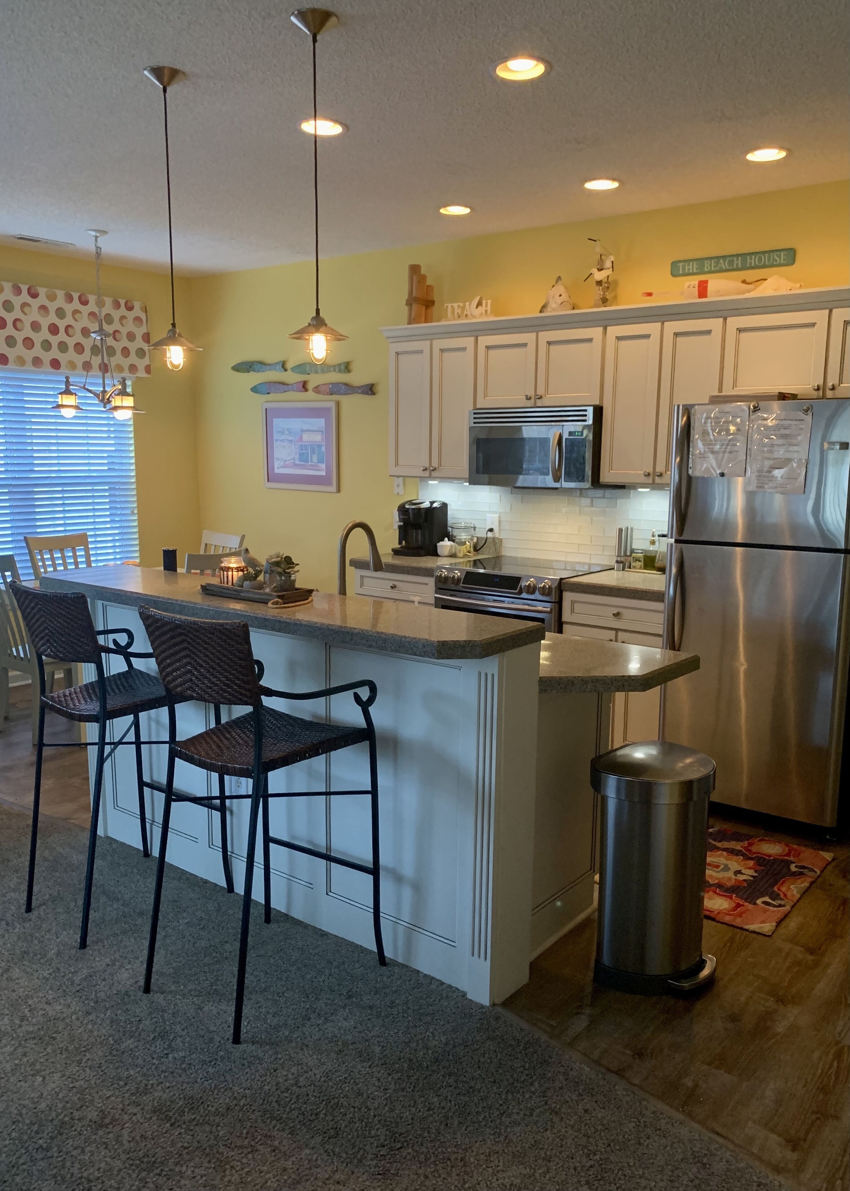 A kitchen with white cabinets, stainless steel appliances, and a central island with bar stools.