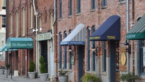 A row of brick buildings with storefronts, including a cafe, a toy store, and a restaurant. - Luxury Fairway Condo Overlooking Two Fairways : Near Beaches - (Leland)