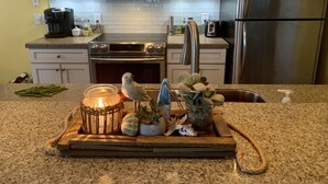 A kitchen with a microwave, oven, and refrigerator. There is a tray with a candle, a plant, and some decorative items on the counter. - Luxury Fairway Condo Overlooking Two Fairways : Near Beaches - (Leland)