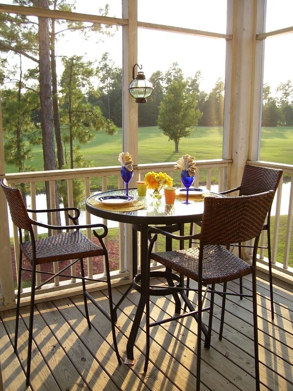 Un patio techado al aire libre con una mesa redonda, sillas de mimbre y vista a un campo de golf.