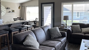 A modern living room with a brown leather sofa, a dining area with a wooden table, and a ceiling fan. - Bridges Bay Ranch style, single story home with 3 bedrooms and 2 bathrooms (Arnolds Park)