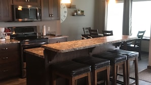 A modern kitchen with a central island, bar stools, wooden cabinets, and a large clock on the wall. - Bridges Bay Ranch style, single story home with 3 bedrooms and 2 bathrooms (Arnolds Park)