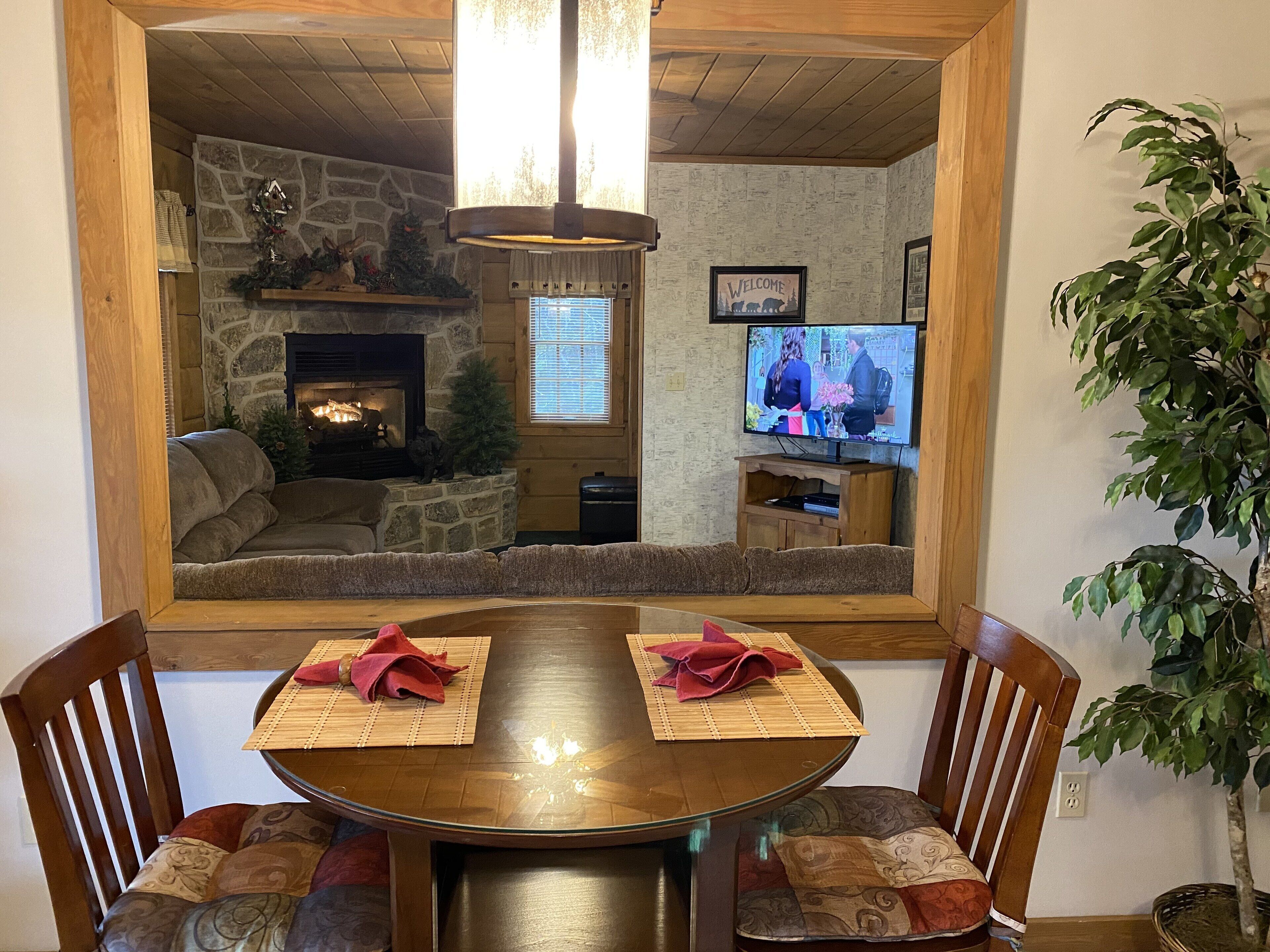 Een gezellige woonkamer met een stenen openhaard, een televisie en een eethoek met een ronde tafel en stoelen.