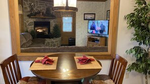 Un salon chaleureux avec une cheminée en pierre, un téléviseur et un coin repas comprenant une table ronde et des chaises.