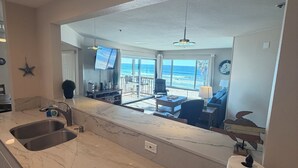 A modern kitchen with a large island, a built-in sink, and a view of a living area with a pool and outdoor furniture. - 5 - STAR -⭐⭐⭐⭐⭐- LUXURY OCEAN FRONT CONDO - JACUZZI - FAMILY FRIENDLY - SLEEPS 6 (San Diego)