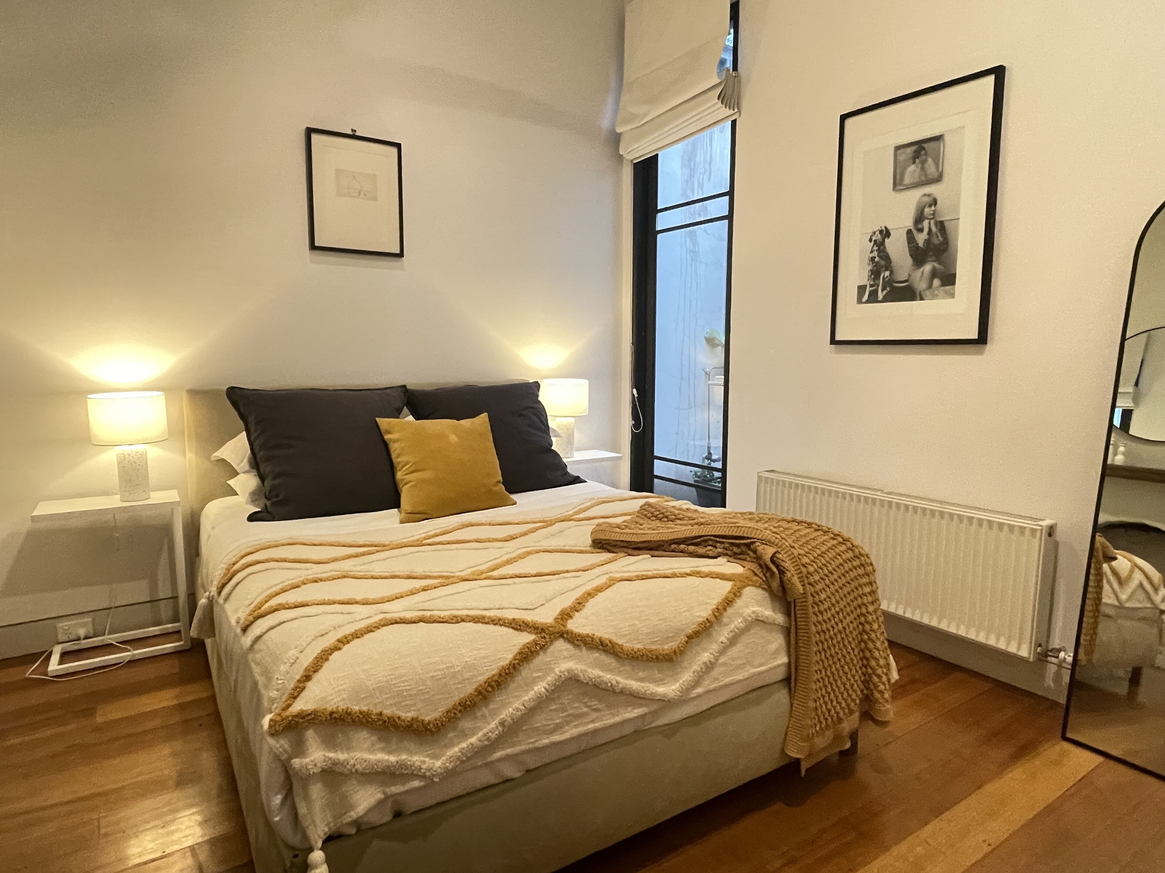A neatly made bed with a white and beige blanket, two bedside lamps, and a framed picture on the wall.