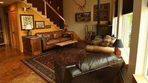 Ein großzügiger Wohnraum mit Treppe, Ledersofas, einem gemusterten Teppich und Wandstücken aus Geweihen.