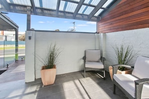 A covered outdoor seating area with two chairs and two potted plants.